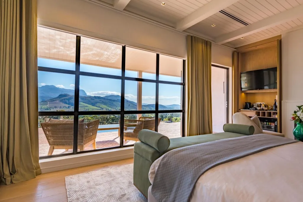 Bedroom with large windows overlooking mountains green ottoman and bed with gray blanket