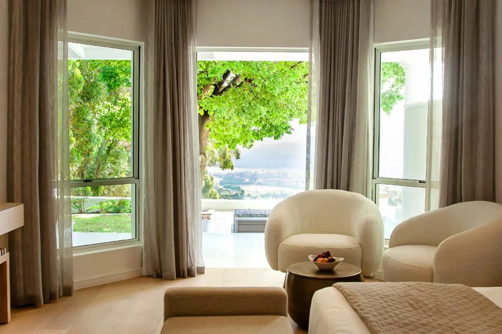 Bright bedroom with large windows overlooking a garden and distant mountains