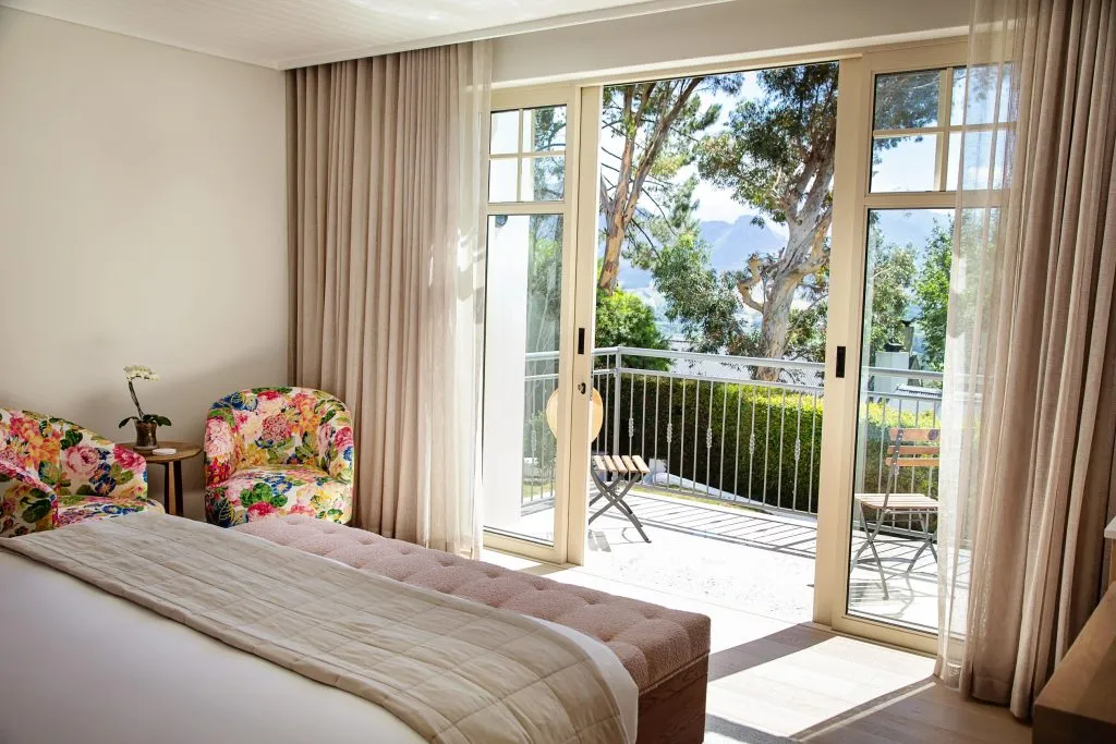 Bedroom with floral chairs large bed and open doors to a garden view
