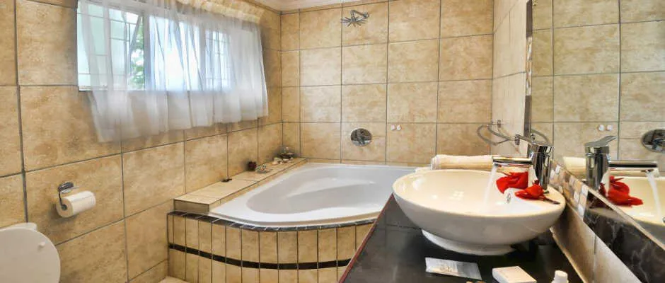 Beigetiled bathroom with white bathtub sink and toilet with a window