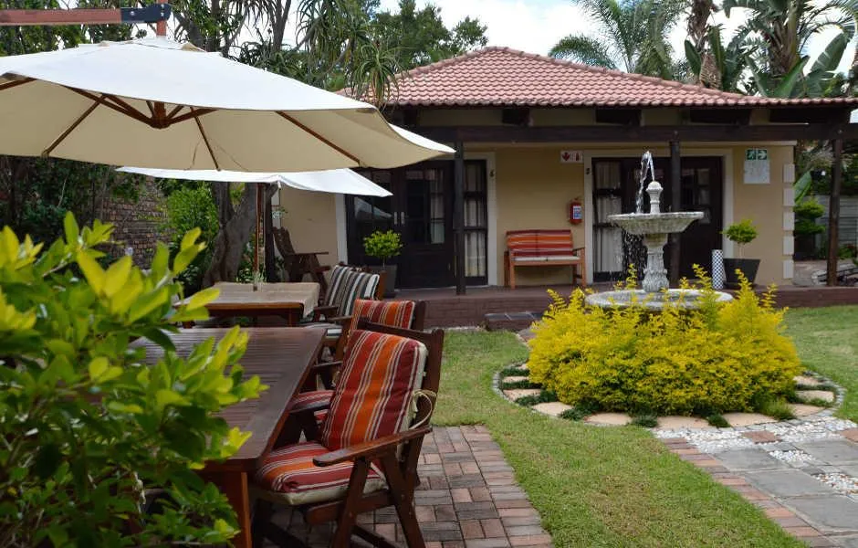 Outdoor seating area with tables chairs and a fountain in a garden