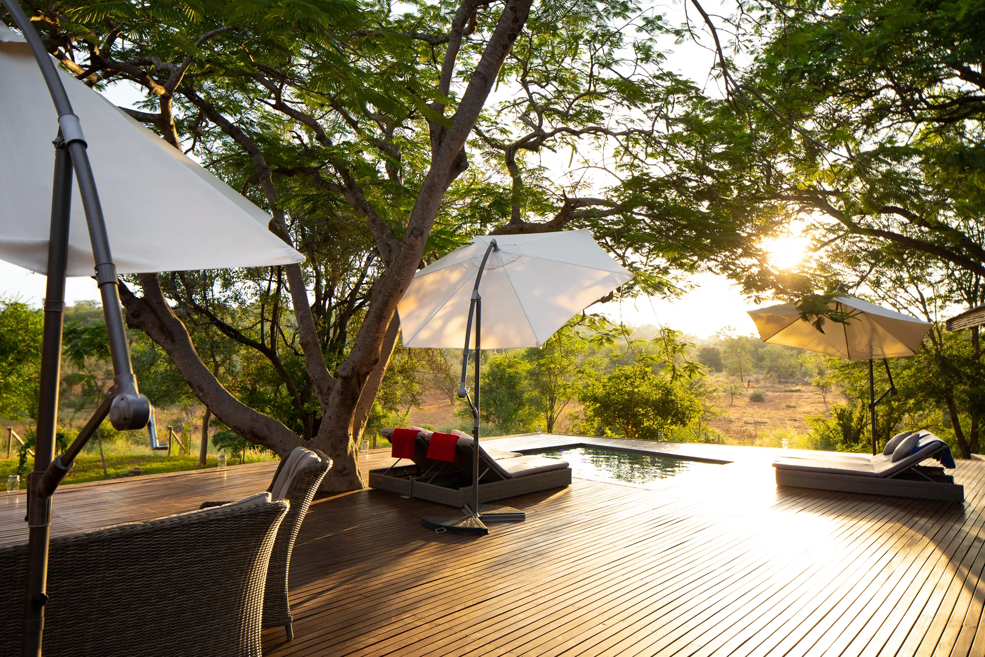 Wooden deck with lounge chairs umbrellas and a pool overlooking a sunset landscape