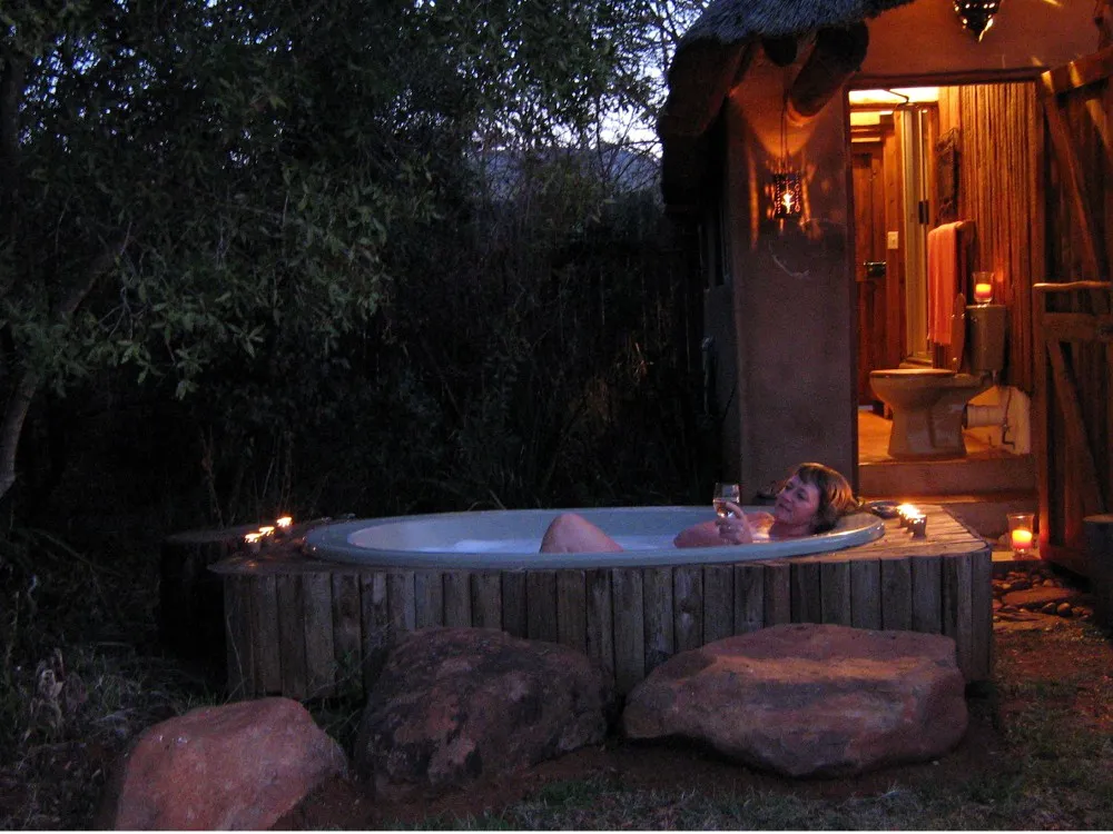 Person relaxing in a wooden hot tub at night with candles and rocks