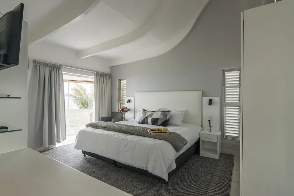 Modern bedroom with large bed white headboard and sliding glass doors to balcony
