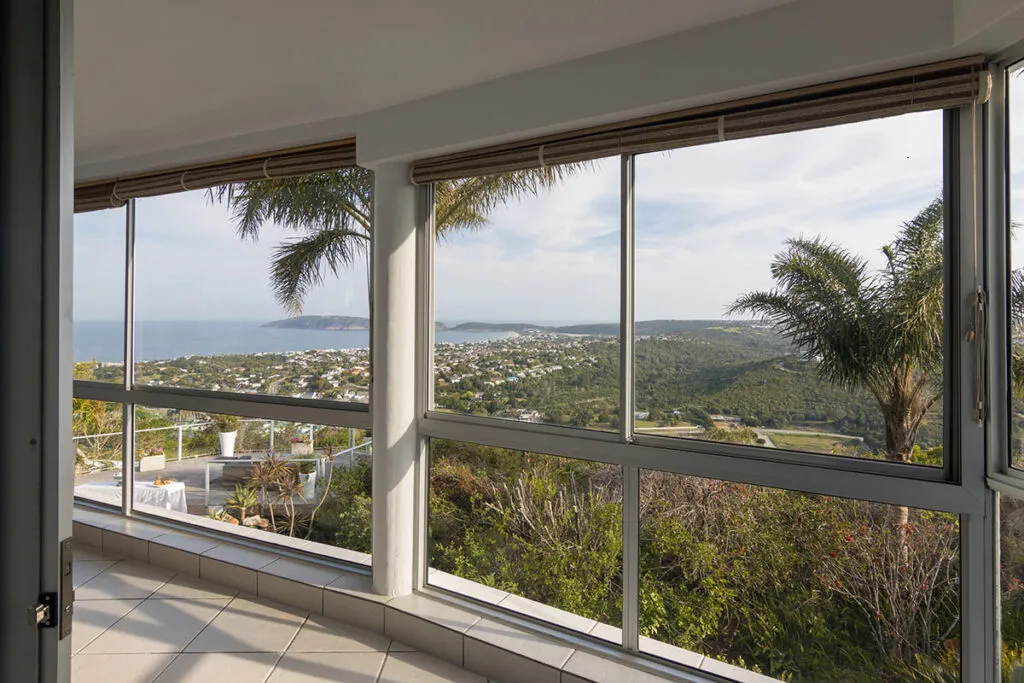 Balcony with large windows overlooking a scenic coastal landscape with greenery and ocean