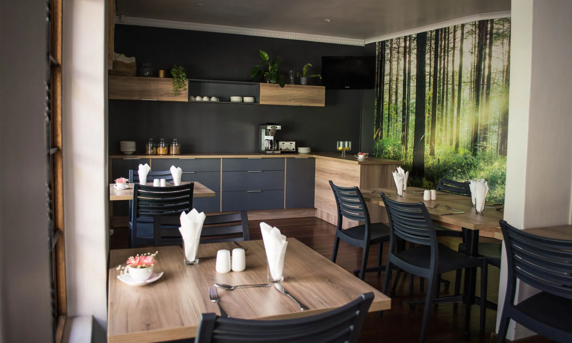 Modern dining area with wooden tables chairs and forestthemed wall mural