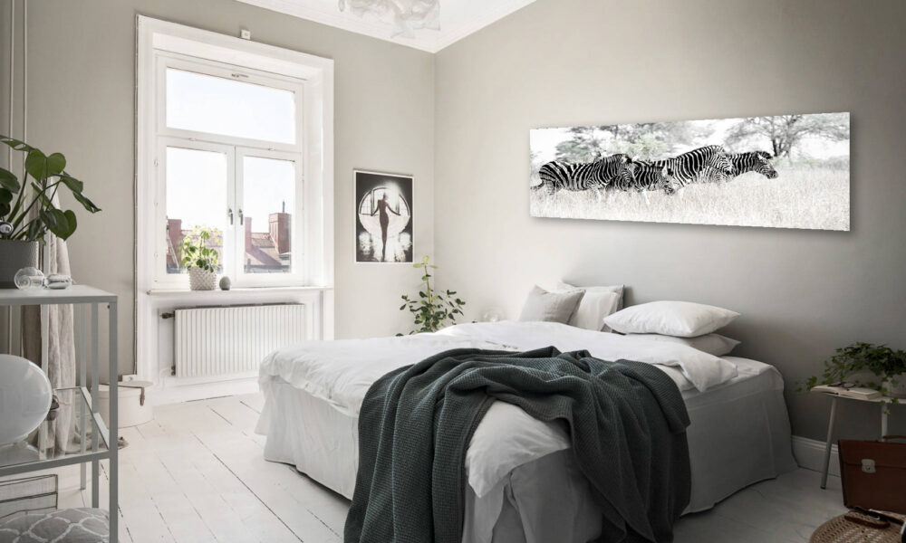Modern bedroom with large zebra artwork above bed, white walls, and wooden floor.