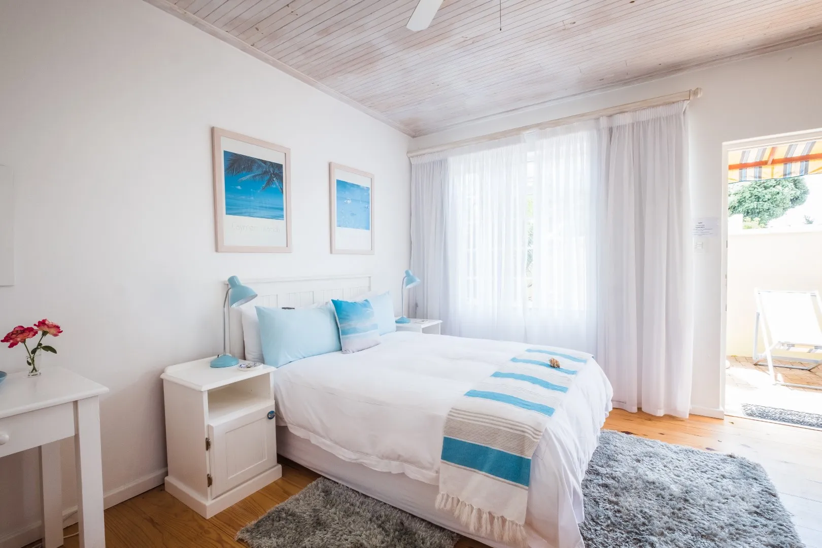 Bright bedroom with white bed blue accents and wooden ceiling