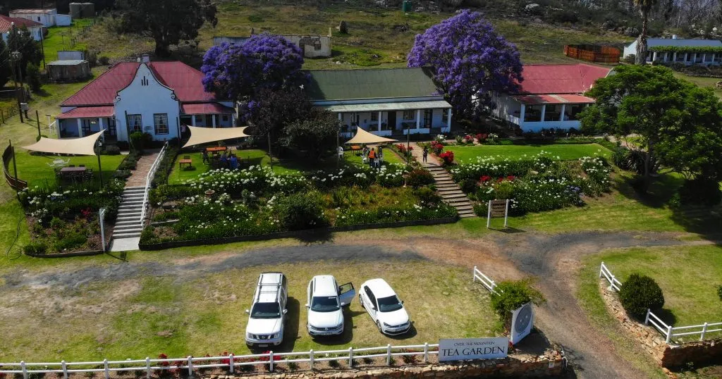 Aerial view of a house with gardens cars and a sign Tea Garden