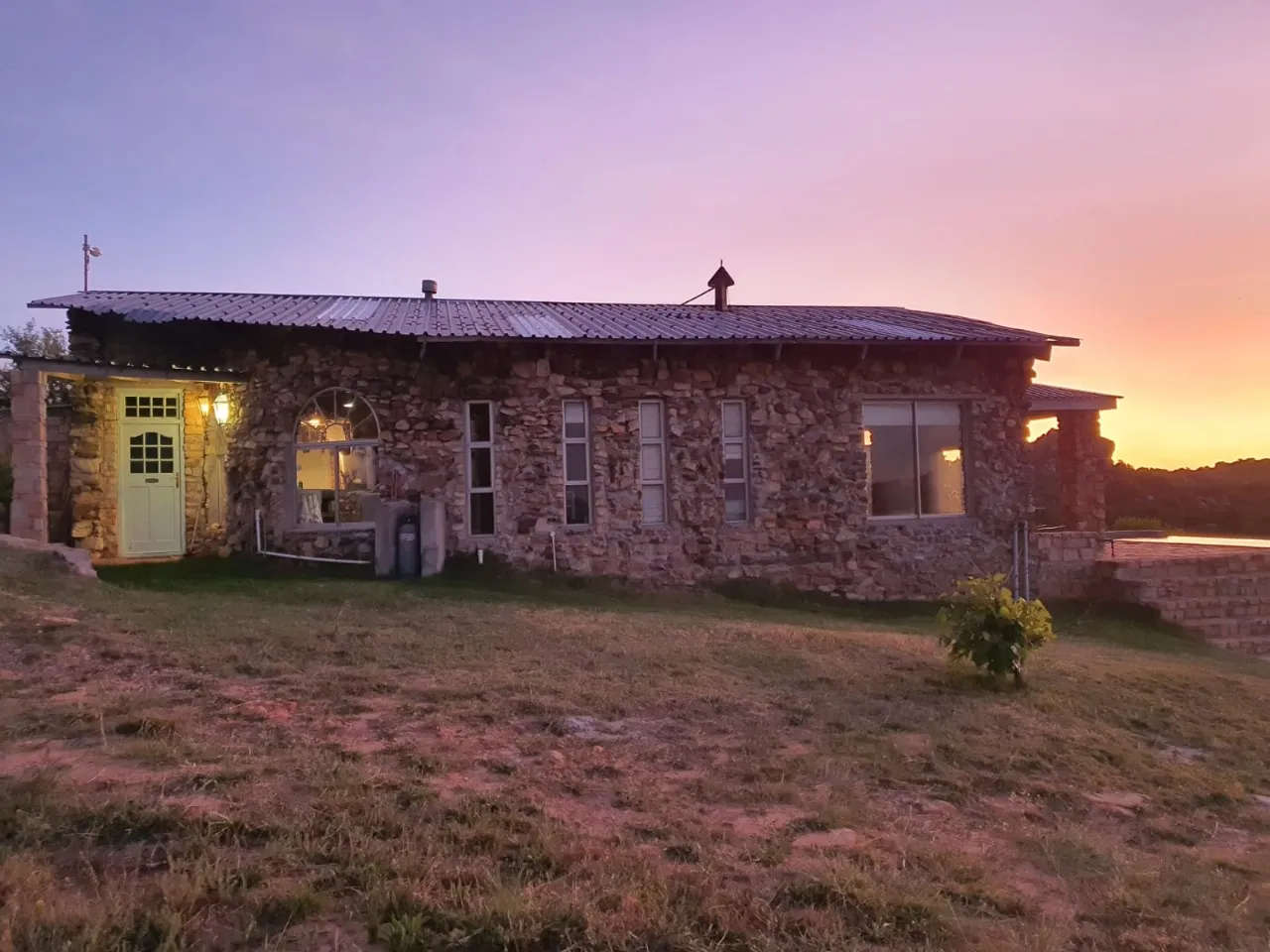 Stone house with a green door at sunset on a grassy hill
