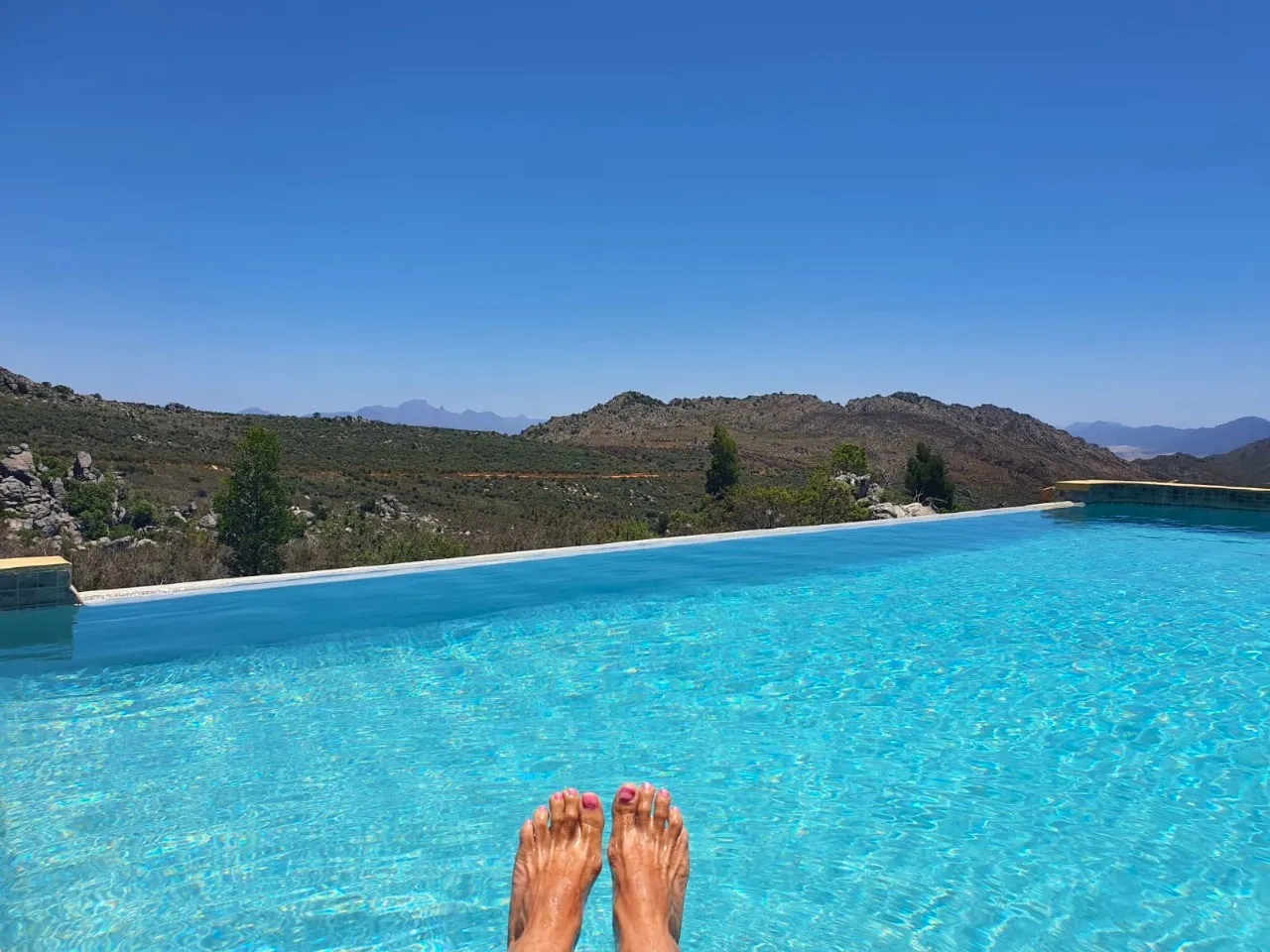 Persons feet in a pool with a scenic mountain view in the background