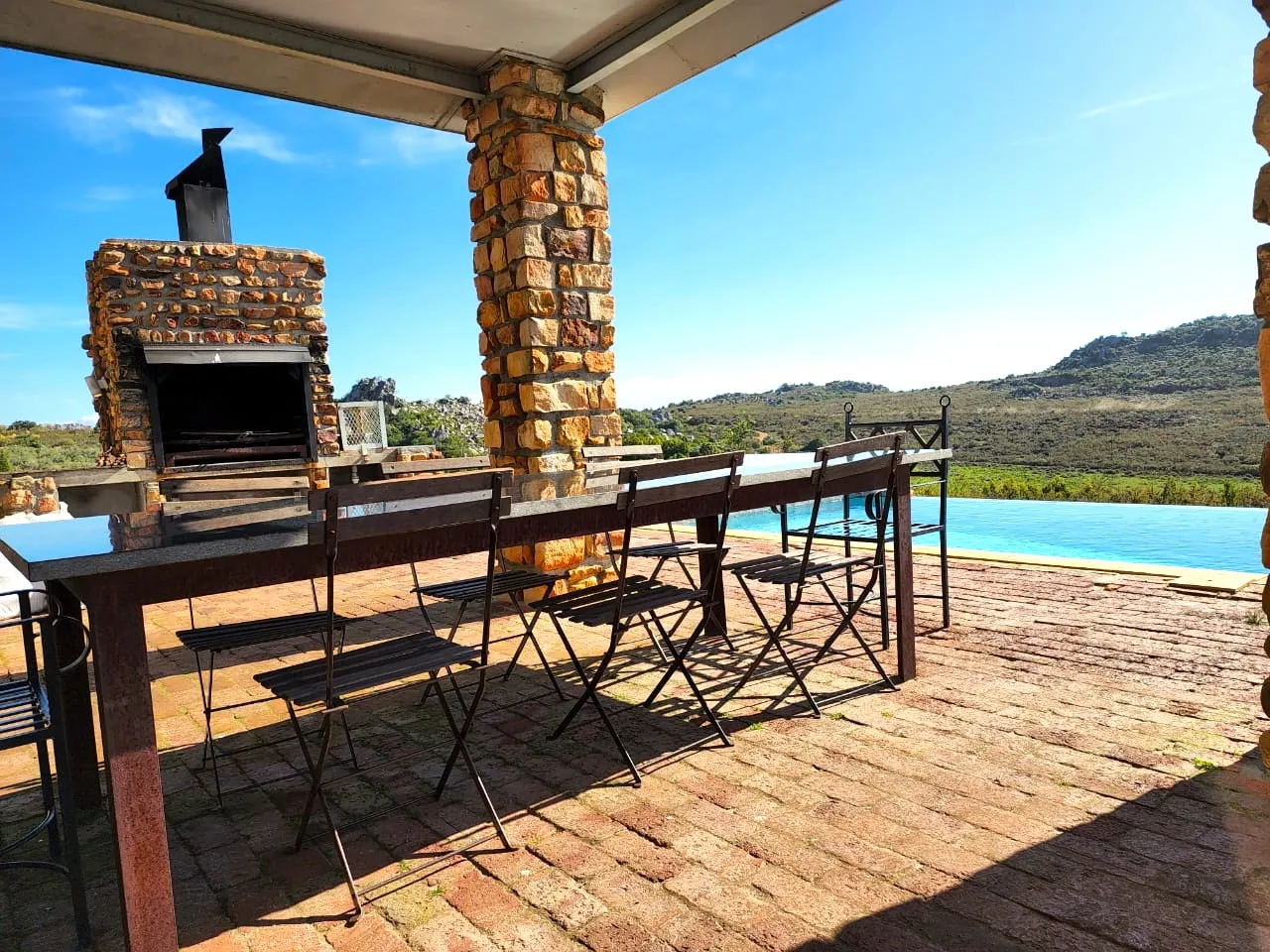 Outdoor patio with stone fireplace dining table chairs and pool view