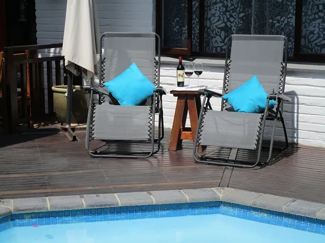 Two lounge chairs with blue cushions by a pool with a wine bottle and glasses