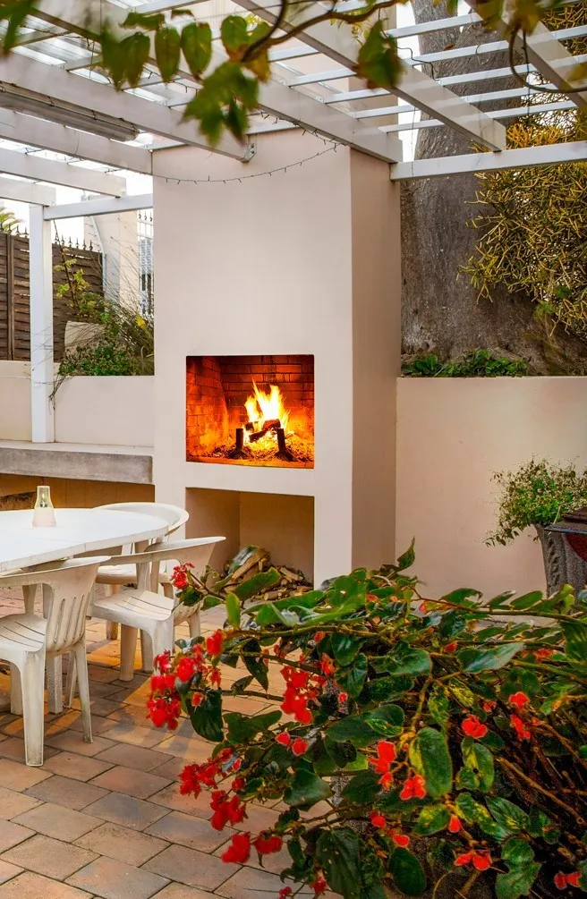 Outdoor patio with lit fireplace white chairs and vibrant red flowers