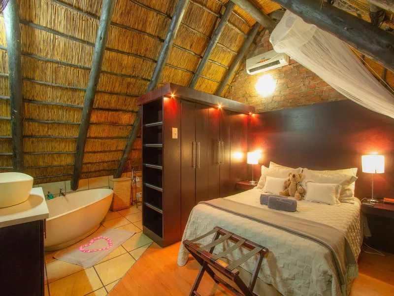 Cozy bedroom with wooden ceiling bed bathtub and warm lighting