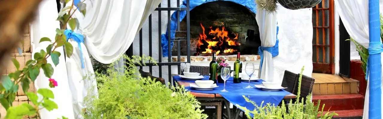 Outdoor dining area with a blue tablecloth and a lit fireplace in the background