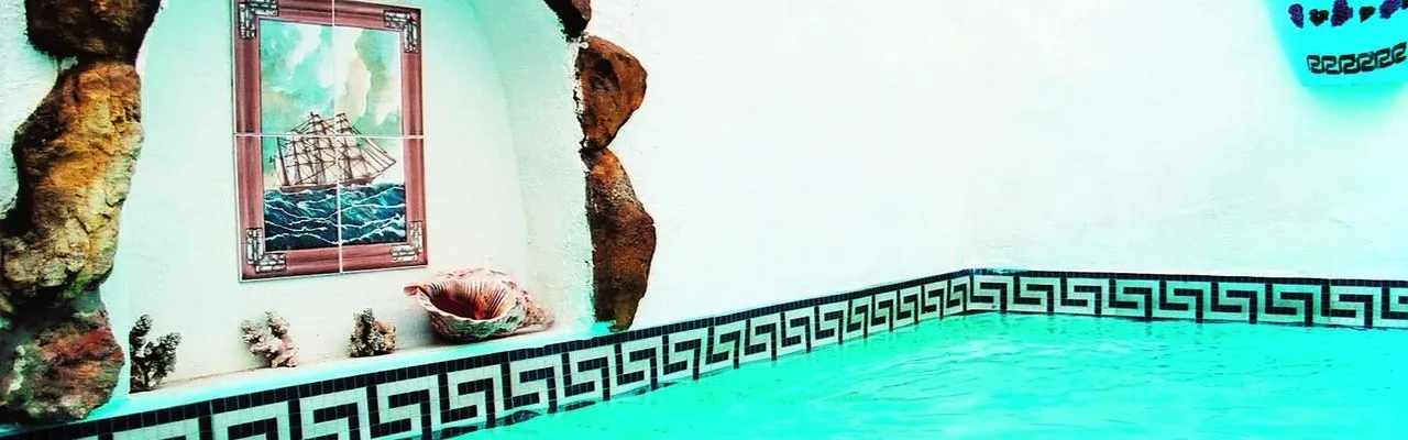 Indoor pool with Greek key border rock formations and a framed ship painting