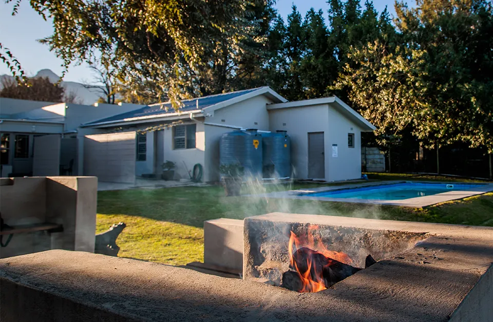 Fire pit in front of a house with a pool and garden