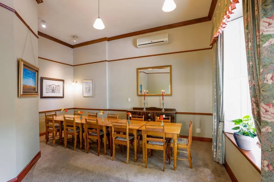 Wooden dining table with chairs in a welllit room with floral curtains