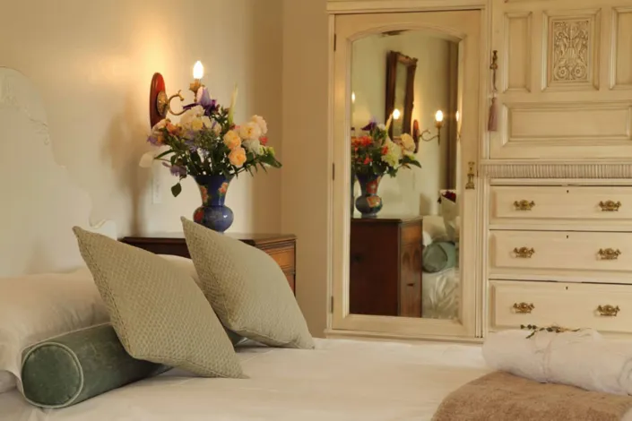 Bedroom with a bed pillows dresser mirror and a vase of flowers