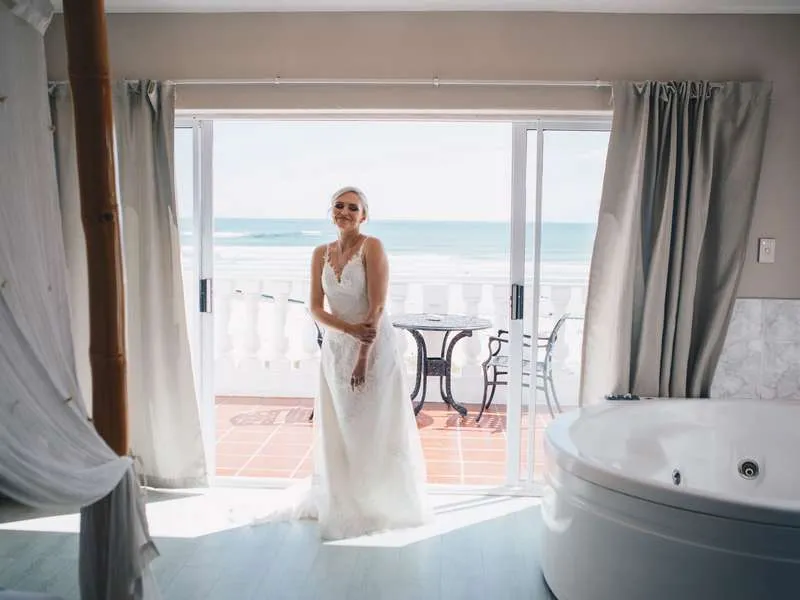 Bride in white dress standing in a room with ocean view and bathtub
