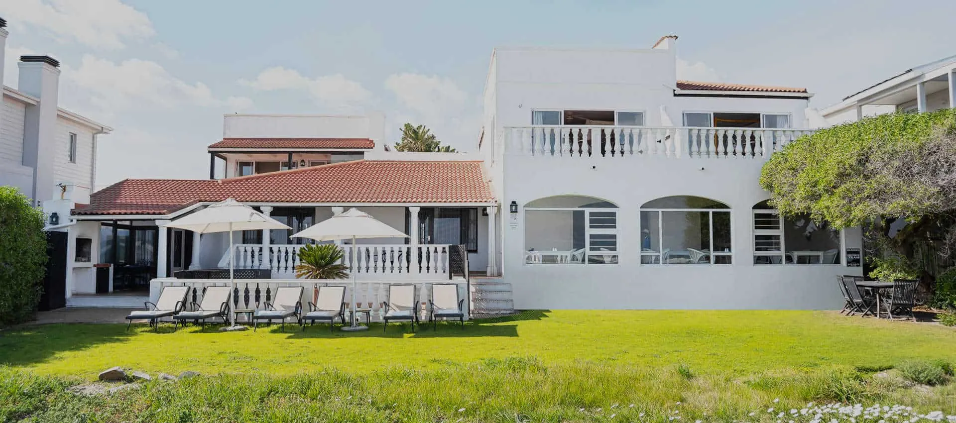 Large white house with red roof lawn and lounge chairs in front