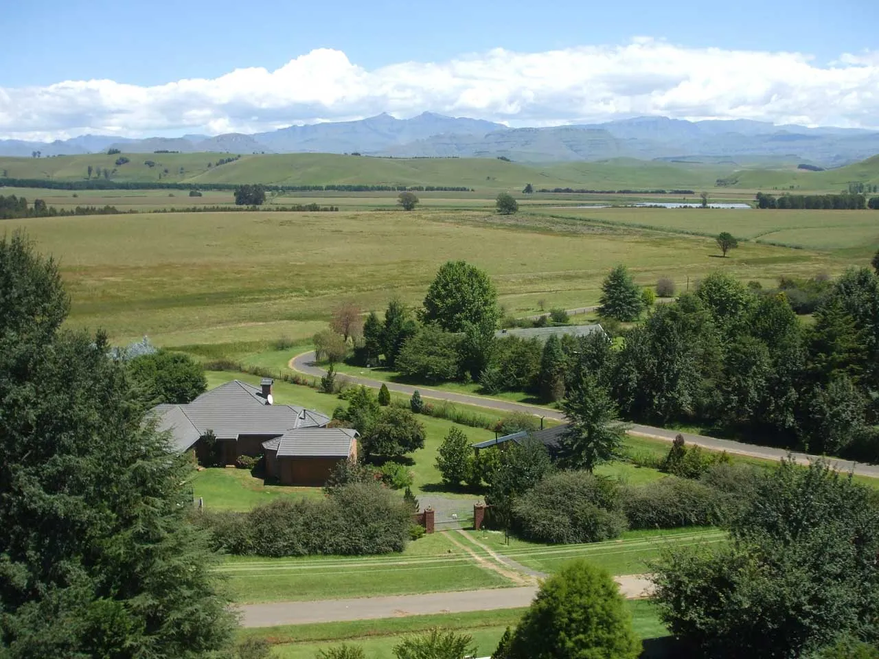 A house surrounded by trees and fields with mountains in the background