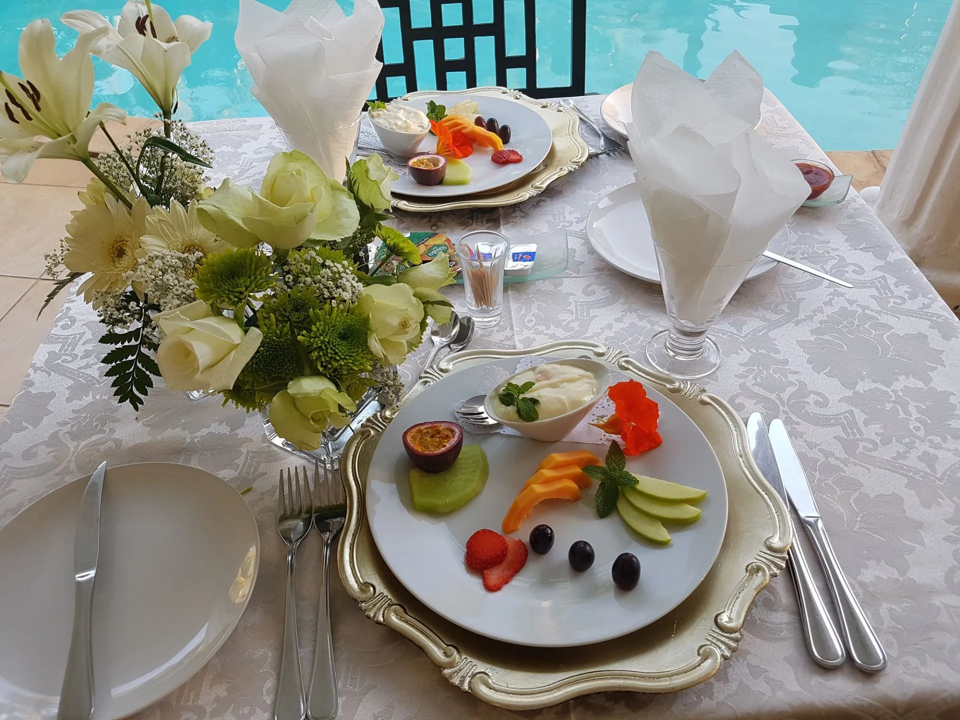 Two plates of fruit with flowers and cutlery on a table by a pool