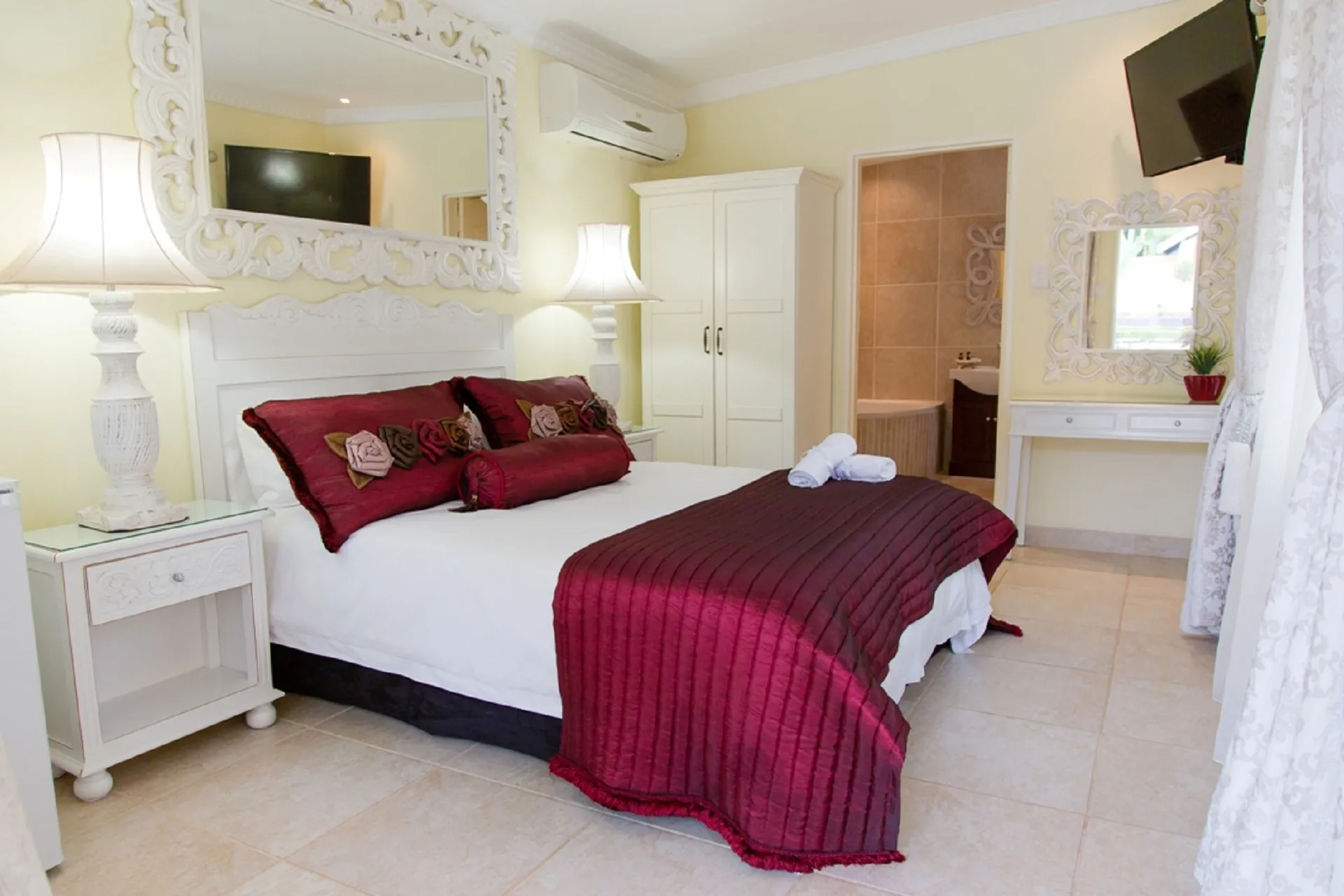Elegant bedroom with white furniture red bedding and an attached bathroom