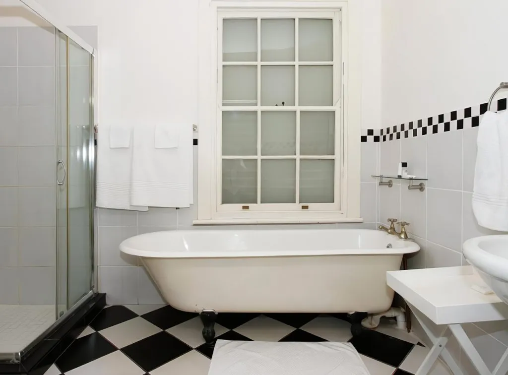 White bathroom with clawfoot tub black and white checkered floor and towels