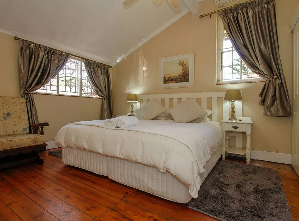 Cozy bedroom with a large bed wooden floor and two windows with curtains