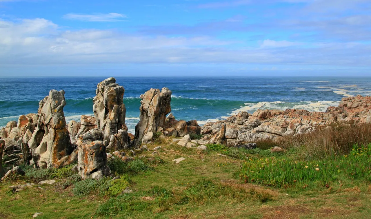 Rocky formations by the ocean with grassy foreground under a blue sky