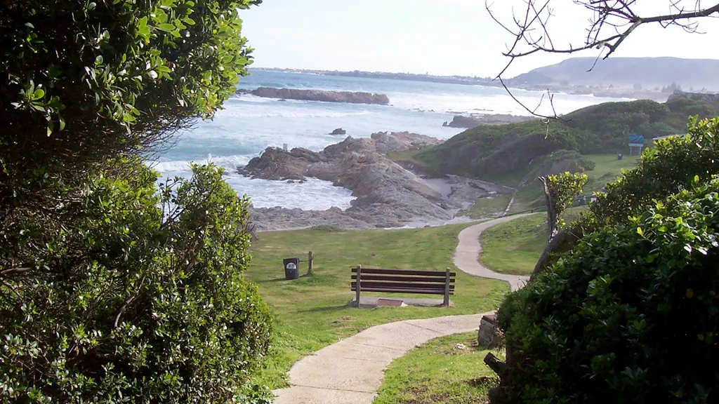 Pathway to a bench overlooking rocky coastline with greenery and ocean waves