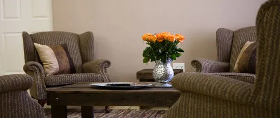 Three armchairs around a wooden table with a vase of orange roses