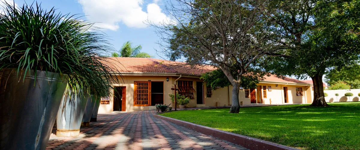Singlestory house with tiled roof large lawn and trees in front