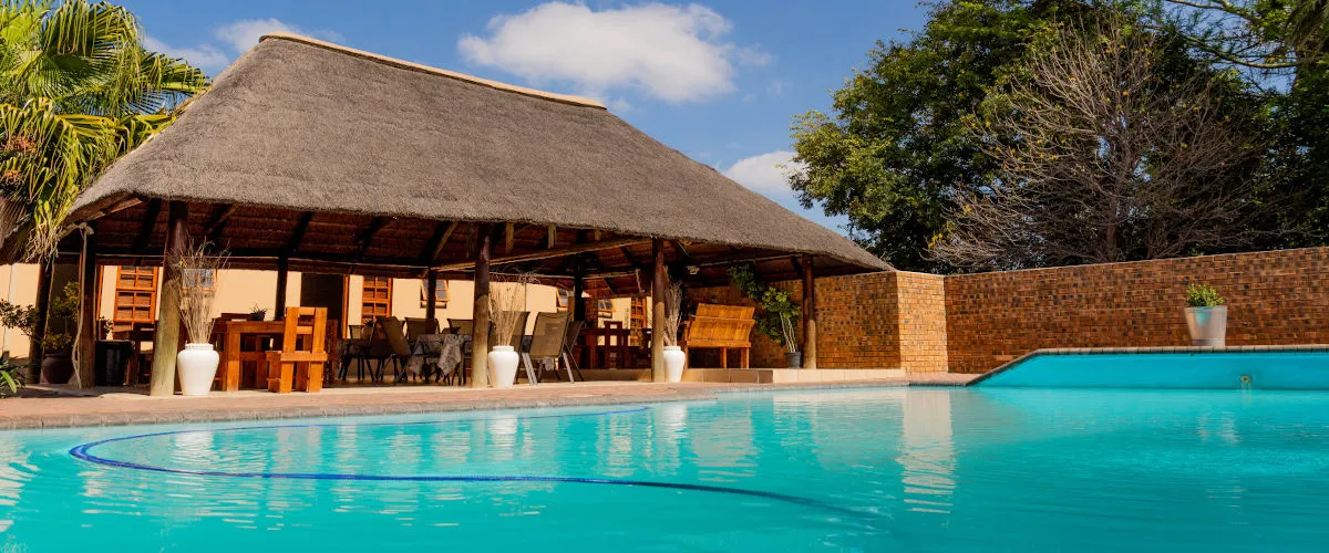Swimming pool with thatchedroof structure and seating area in the background