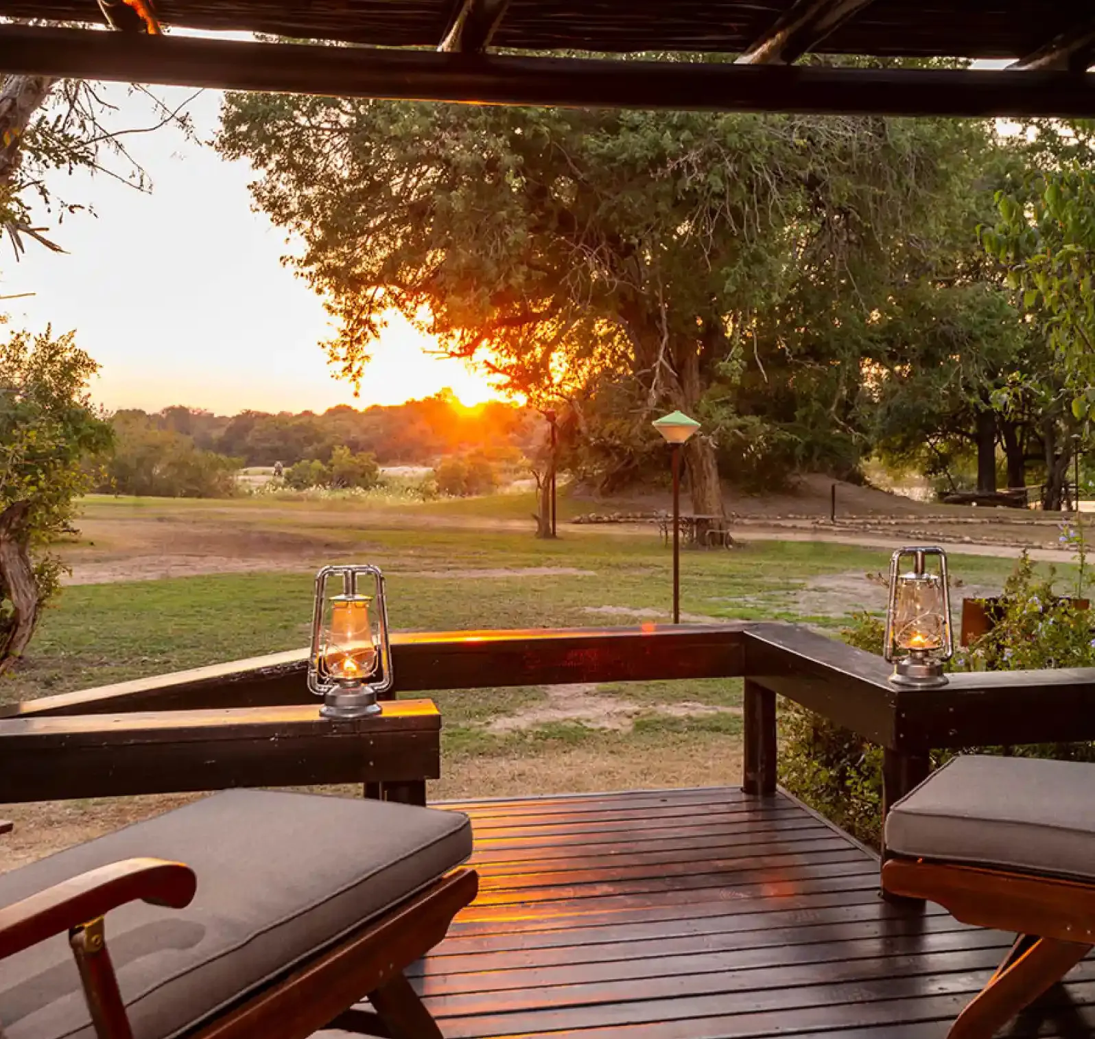 Two chairs on a wooden deck at sunset with lanterns and trees in background