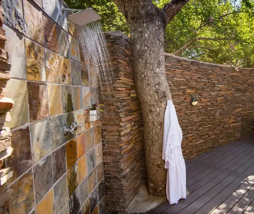 Outdoor shower with stone wall tree trunk and white robe hanging nearby