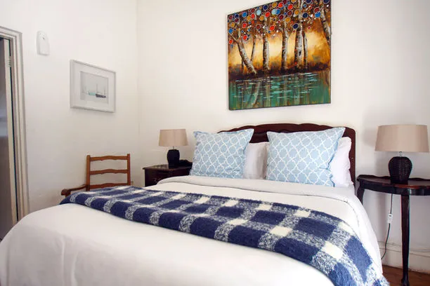 Cozy bedroom with a neatly made bed nightstands lamps and a tree painting