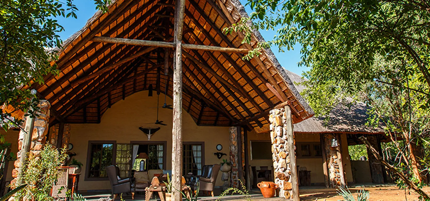 Rustic lodge with thatched roof and outdoor seating surrounded by greenery
