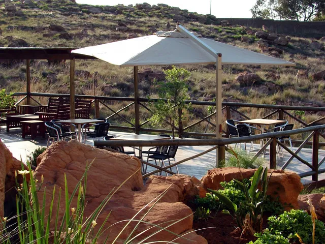 Outdoor seating area with tables chairs and a large umbrella on a rocky patio