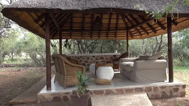 Outdoor seating area under a thatched roof with stone walls and greenery