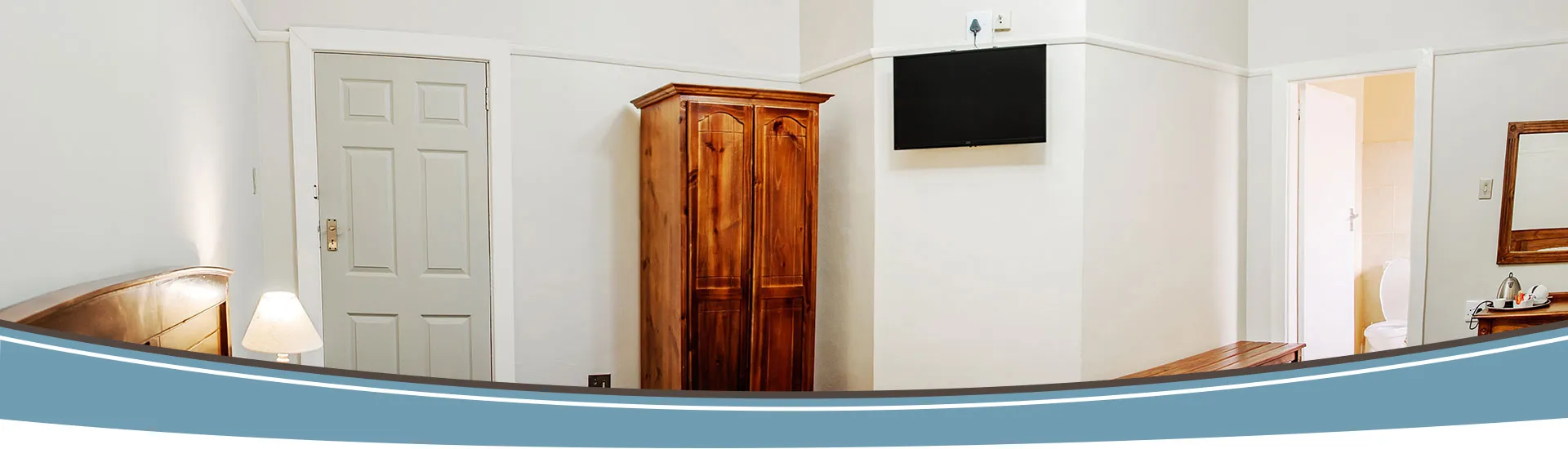 Panoramic view of a simple bedroom with wooden furniture and a TV