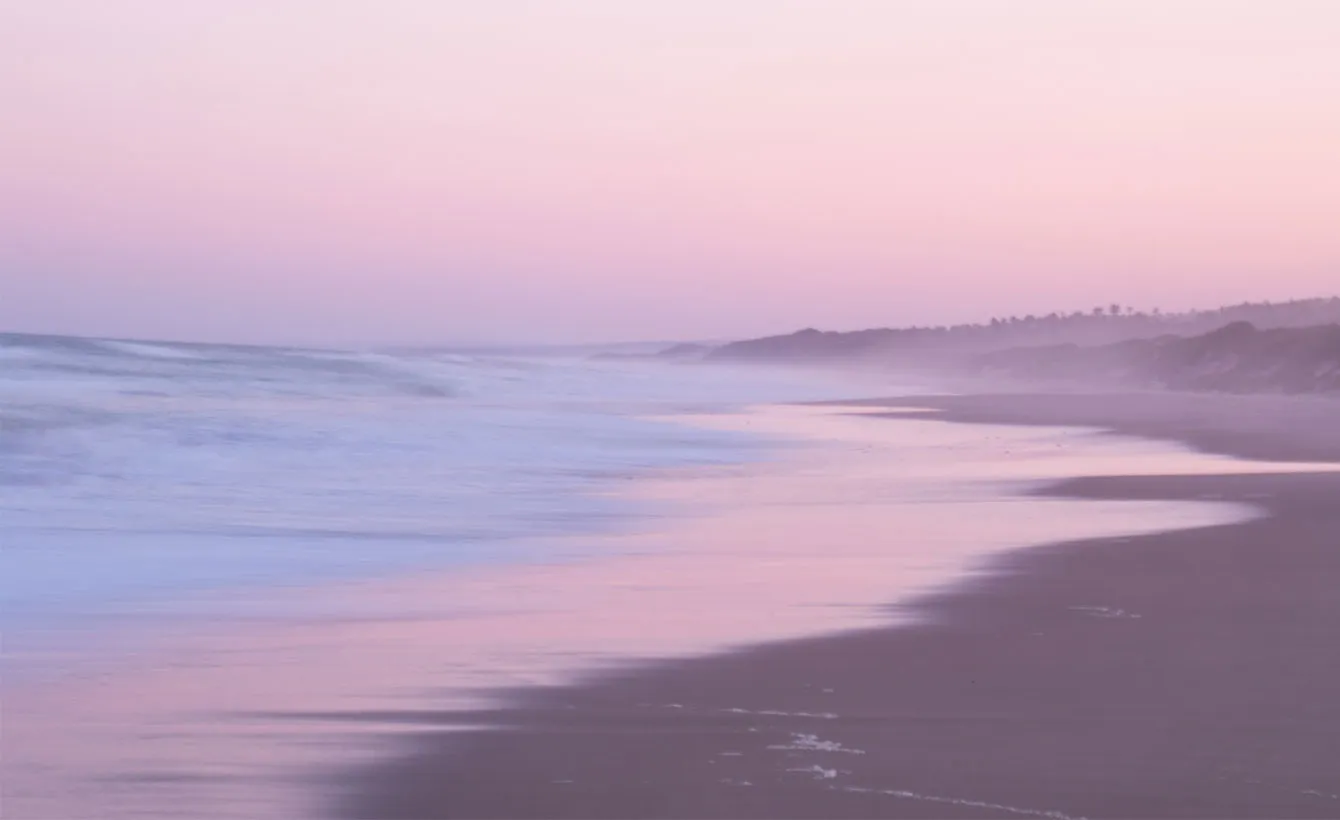 Beach at sunset with gentle waves and soft pink sky