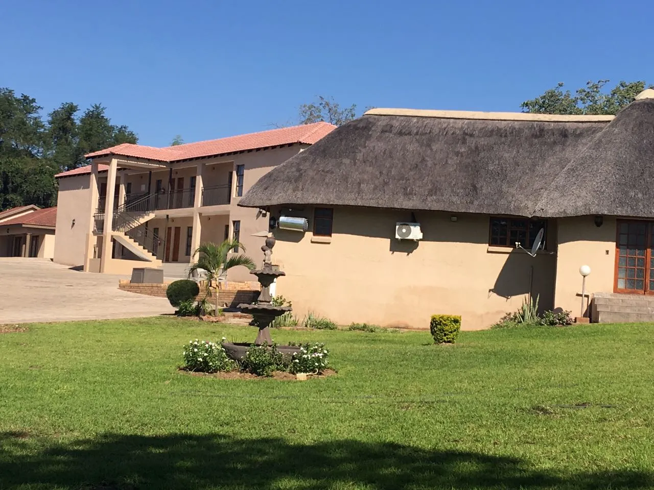 Traditional thatchedroof house with a fountain in a grassy yard