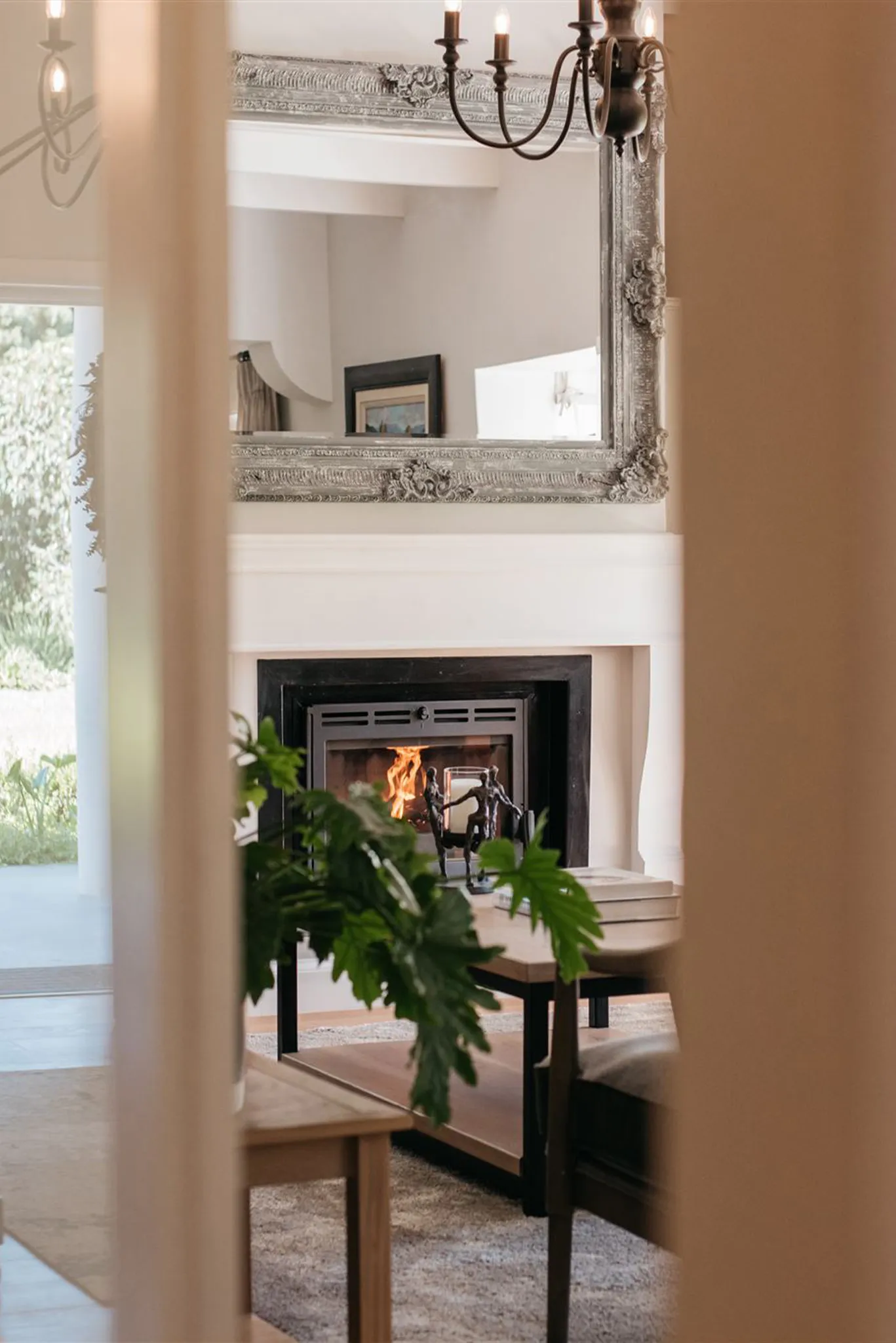 Cozy living room with lit fireplace mirror and plants