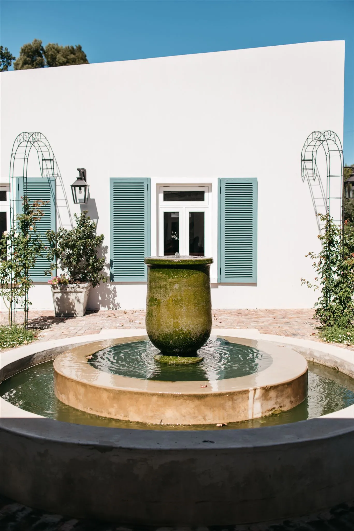Green fountain in front of a white building with bluegreen shutters