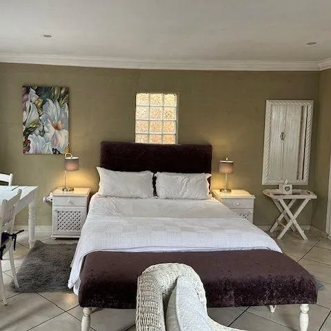 Bedroom with large bed side tables lamps and a floral painting on the wall