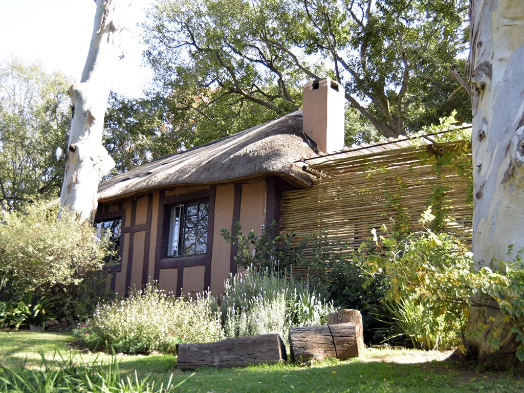 Thatched cottage with garden trees and wooden fence in a natural setting