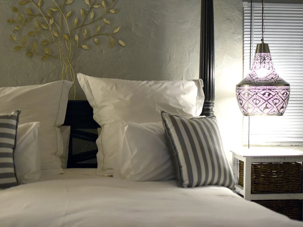 Bed with white pillows striped pillow and a decorative wall lamp